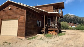 A two-story wooden cabin with a garage, a balcony, and a mountain backdrop. - KXDJ Riverside 1 on the River (Red River)