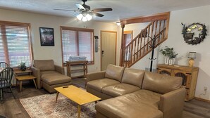 A living room with a brown leather sofa, a wooden coffee table, a patterned rug, a ceiling fan, and a staircase. - KXDJ Riverside 1 on the River (Red River)