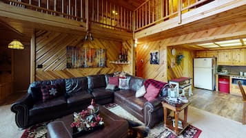 Un interior acogedor de cabaña con un sofá de cuero, una mesa de comedor y una zona de cocina.