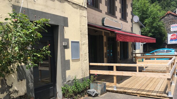 A building with a wooden deck, a black door, and a red awning.