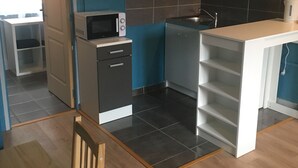 A modern kitchen with a microwave, dishwasher, and sink. There is a wooden dining table and a chair. The walls are painted teal, and the floor is tiled.