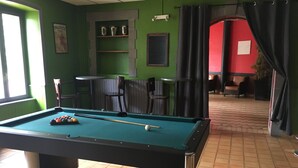 A pool table in a room with green walls, a red accent wall, and a tiled floor. There are chairs and a shelf with items on it.