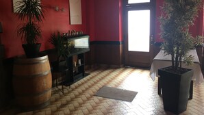A room with a red wall, a wooden barrel, a potted plant, a small table, and a door with a bright window.