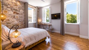 A bedroom with a stone wall, wooden flooring, a bed, a desk, and a TV. - Acanthus blue (Corfu)