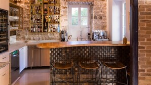 A modern kitchen with a stone wall, bar area, and hanging light fixtures. - Acanthus blue (Corfu)