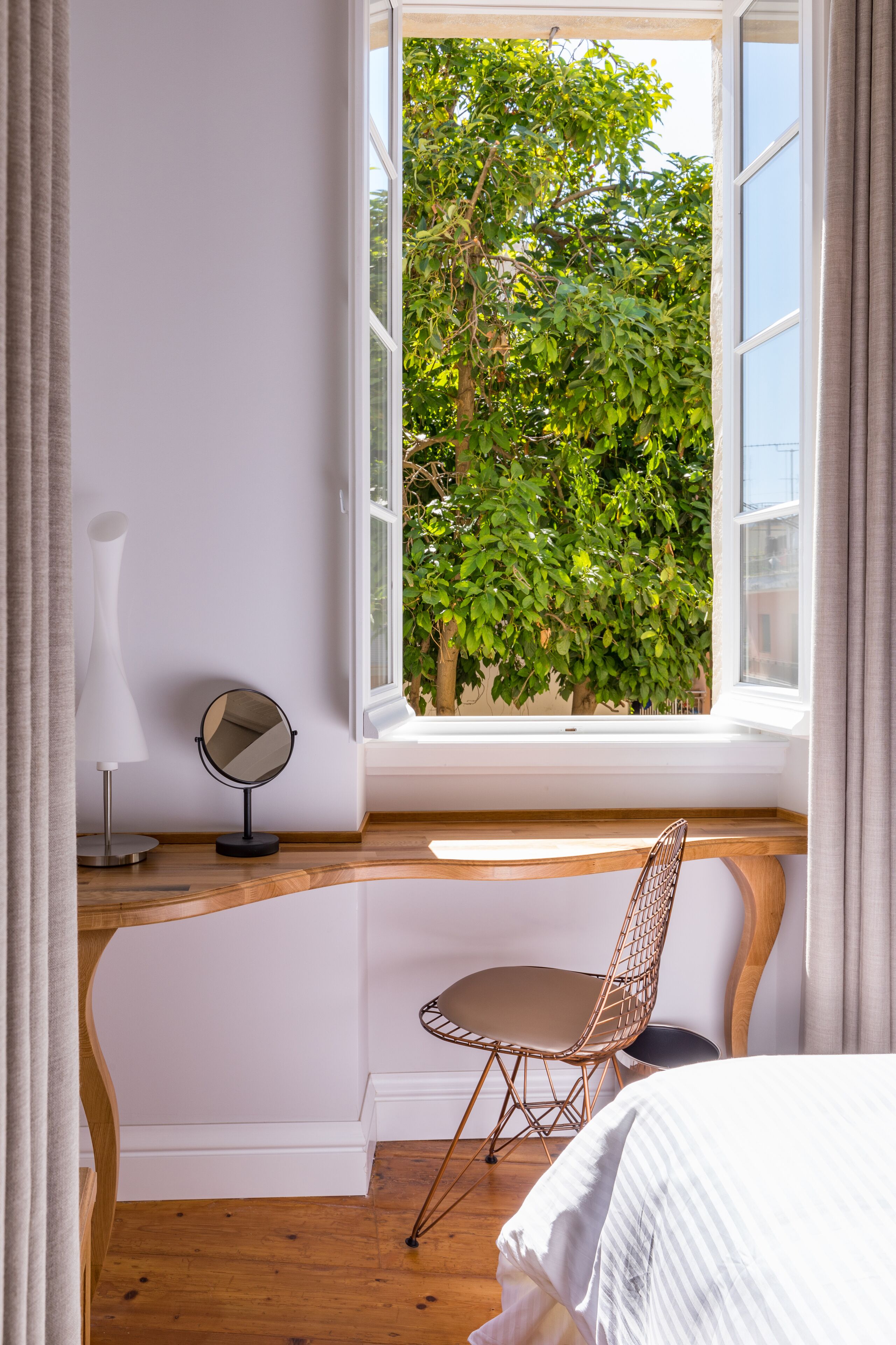 A bedroom with a large window, a wooden desk, a chair, and a bed.