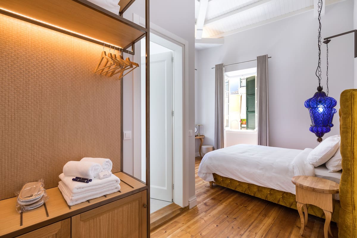 Habitación de hotel con cama, muebles de madera, lámpara colgante y vistas al exterior.