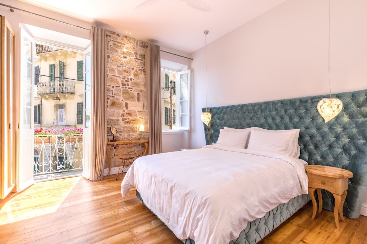 Un dormitorio con una cama grande, una pared de piedra y un balcón con vistas a edificios.