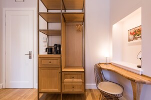 A compact room with a wooden cabinet, a desk, a chair, and a wall-mounted shelf with a picture.