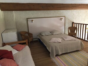 A bedroom with a wooden ceiling, a bed with a white headboard, a small white bedside table, a wicker chair, a striped rug, and a wooden railing. - Villa with a private pool and fenced-in yard, a 10-minute walk from the beach (Bormes-les-Mimosas)