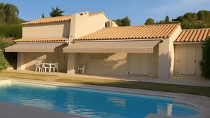 Una casa de dos pisos con piscina, mobiliario exterior y un patio cubierto.