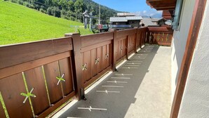 A balcony with a wooden railing, a view of a green hillside, and a building in the background. - Cozy 2-bed apt at ski slopes with parking and WiFi (Flumet)