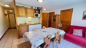 A compact kitchen with wooden cabinets, a microwave, and a dishwasher. There is a dining table with chairs and a red sofa in the living area. - Cozy 2-bed apt at ski slopes with parking and WiFi (Flumet)