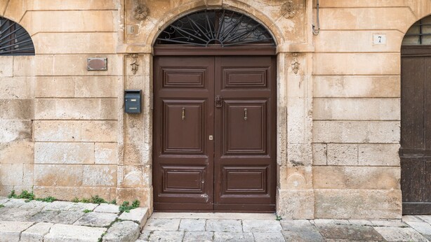 A large, ornate double door with a decorative arch above it, set in a stone building. - Le Cupole -  Mosaico con Terrazza by Wonderful Italy (Ostuni)