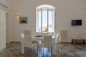 Un coin repas comprenant une table, des chaises, un radiateur, un téléviseur et une fenêtre donnant sur la ville.