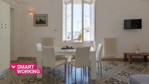 A modern dining area with a white table and chairs, a large window with a view, and a mounted TV on the wall. - Le Cupole -  Mosaico con Terrazza by Wonderful Italy (Ostuni)