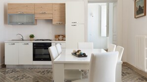 A modern kitchen with white cabinetry, a built-in oven, and a dining area with a white table and chairs. - Le Cupole -  Mosaico con Terrazza by Wonderful Italy (Ostuni)