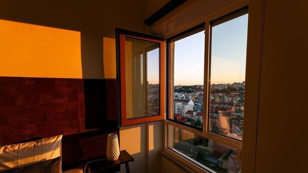 Een slaapkamer met een groot raam, een bed, een klein tafeltje en een lamp.