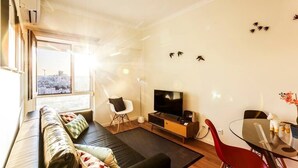 Een moderne woonkamer met een bank, een televisie, een eettafel met stoelen en uitzicht op de stad.