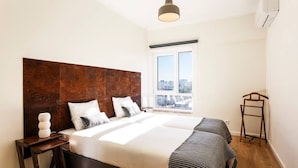 Een moderne slaapkamer met een groot bed, een houten hoofdbord, een nachtkastje, een hanglamp en een raam met uitzicht op de stad.