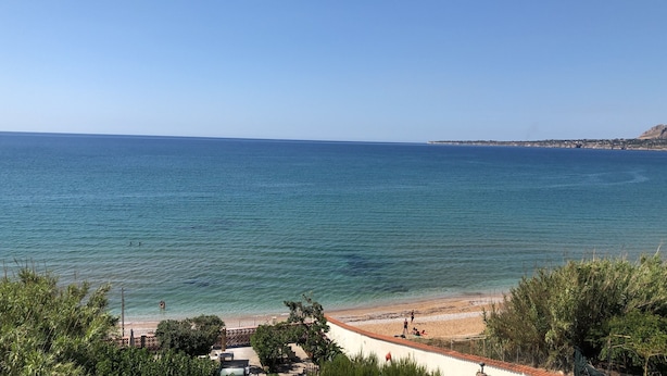Eine Küstenansicht mit Strand, klarem Wasser und weiter Küste im Hintergrund.