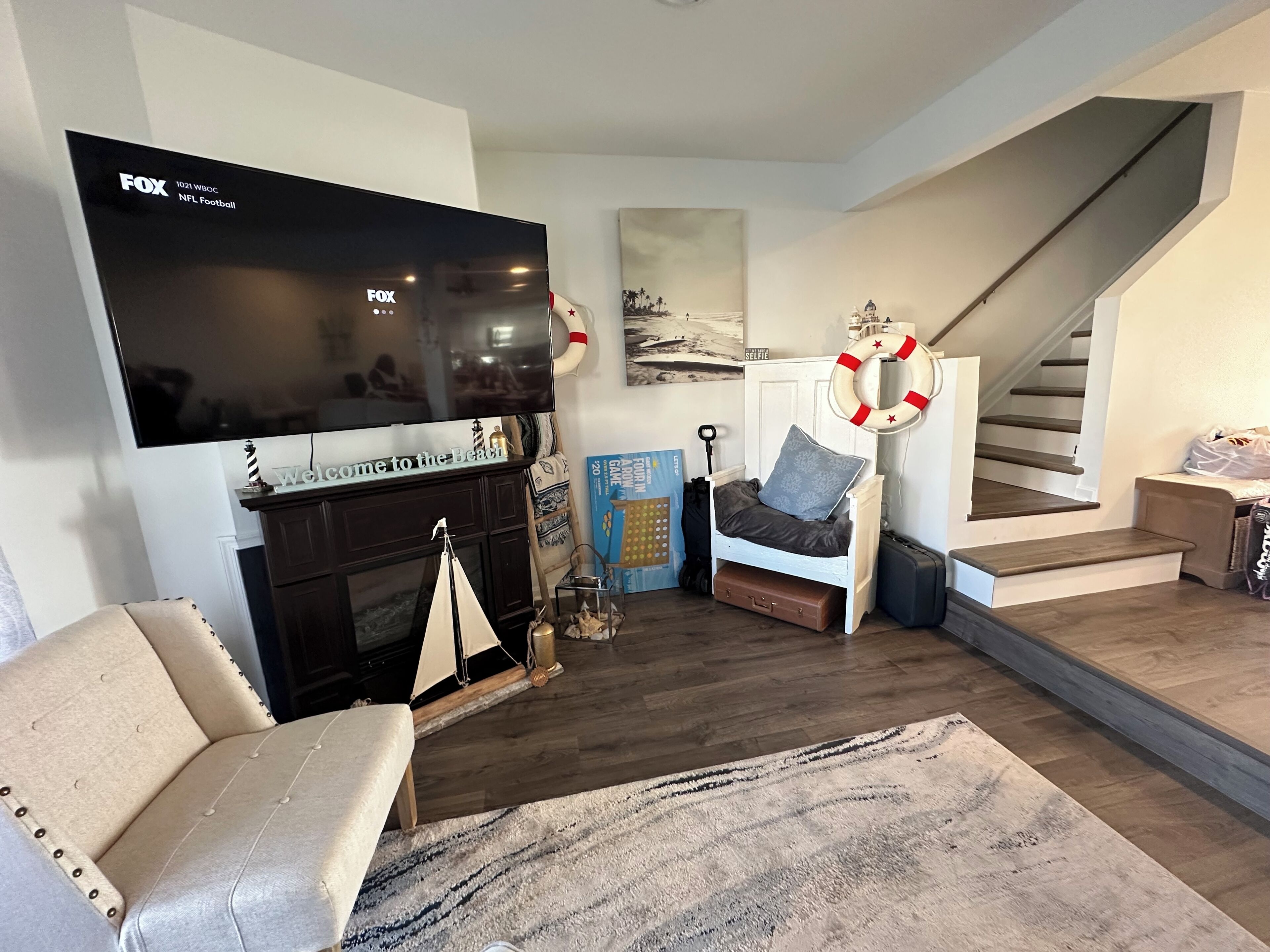 A living room with a television, a sofa, a chair, a small table, a rug, and a staircase.
