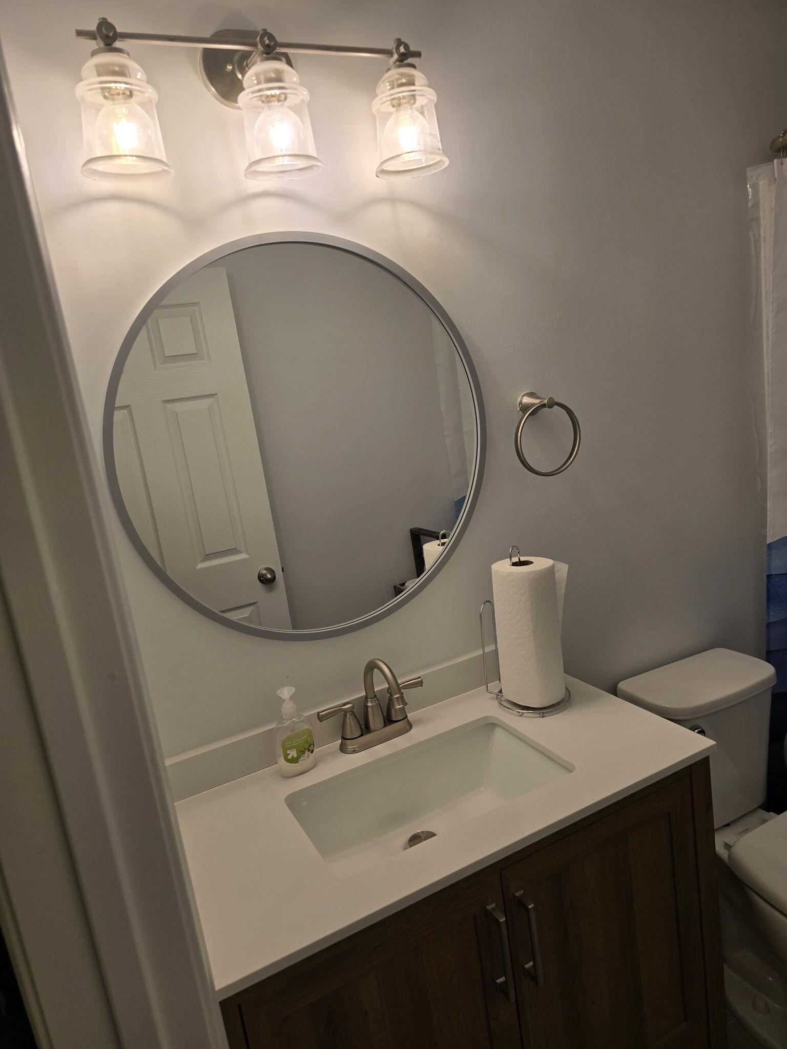 Ein Badezimmer mit rundem Spiegel, Waschbecken, Toilette und Handtuchhalter.