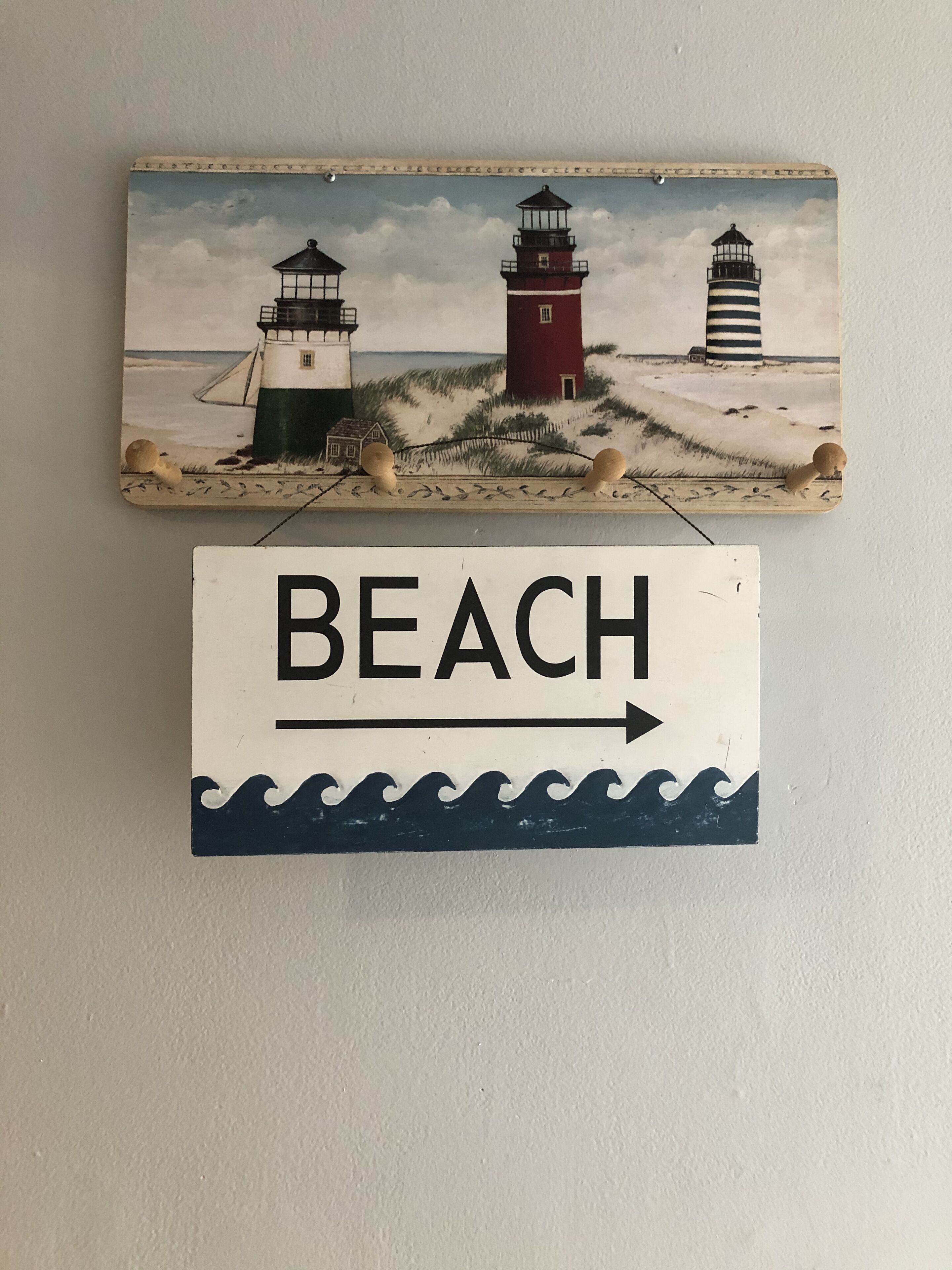 Ein an der Wand befestigtes Schild zeigt drei Leuchttürme und eine Strandansicht, mit einem Pfeil, der nach rechts weist.