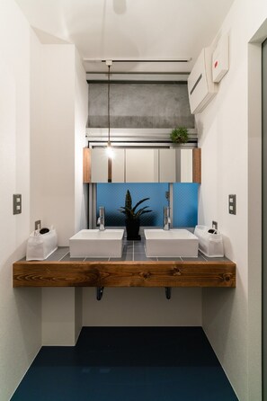 Casa de banho moderna com duas pias, bancada de madeira, parede com detalhes em azul e luminária suspensa.