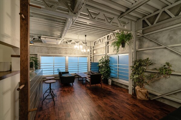 Um quarto amplo com piso de madeira, área de bar e grandes janelas com vidro azulado.
