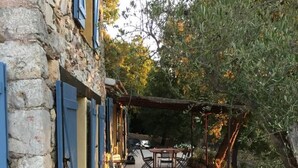 Ein Gebäude aus Stein mit blauen Fensterläden, einer gefliesten Terrasse, Gartenmöbeln und einer Pergola mit Kamin.