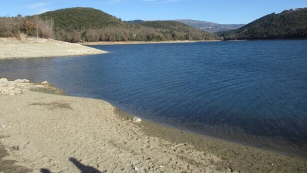 Ein ruhiger See mit einem Sandstrand und Hügeln im Hintergrund.