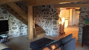 Ein rustikales Interieur mit Steinwand, Holzbalken, einer Treppe, einem Fernseher und einem Sofa.