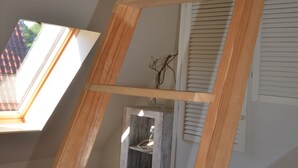 Eine Holzleiter in einem Raum mit schrägem Dach, einem Fenster und einer Tür mit Ablagefläche.