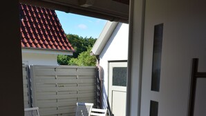 Blick durch eine Tür in einen Patio-Bereich mit Tisch und Stühlen, einer Holzbank und einem weißen Zaun.