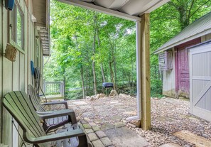 A covered patio with Adirondack chairs, a stone pathway, and a view of a wooded area. - Creekside | Hot Tub | Wood Burning Fireplace | Fire Pit | Wifi (Gatlinburg)