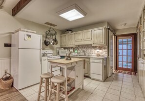 A kitchen with white cabinets, a refrigerator, a microwave, a stove, and a sink. There are two stools and a small island with a sink. - Creekside | Hot Tub | Wood Burning Fireplace | Fire Pit | Wifi (Gatlinburg)
