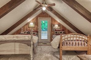 A cozy attic bedroom with two wooden beds, a ceiling fan, and a view of greenery through a door. - Creekside | Hot Tub | Wood Burning Fireplace | Fire Pit | Wifi (Gatlinburg)