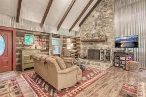 A cozy living room with a stone fireplace, wooden beams, and a television mounted on the wall. - Creekside | Hot Tub | Wood Burning Fireplace | Fire Pit | Wifi (Gatlinburg)