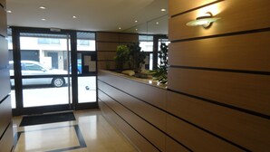 A hotel reception area with a glass door, a reception desk, and a small indoor garden. - One-Bedroom Apartment, good standard,  with balcony and parking (Lyon)