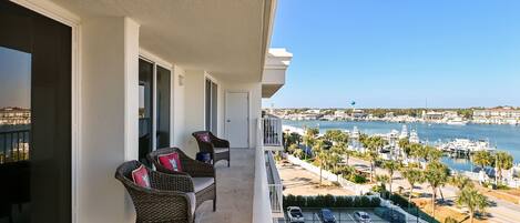 A balcony with wicker furniture, a tennis court, and a marina view.