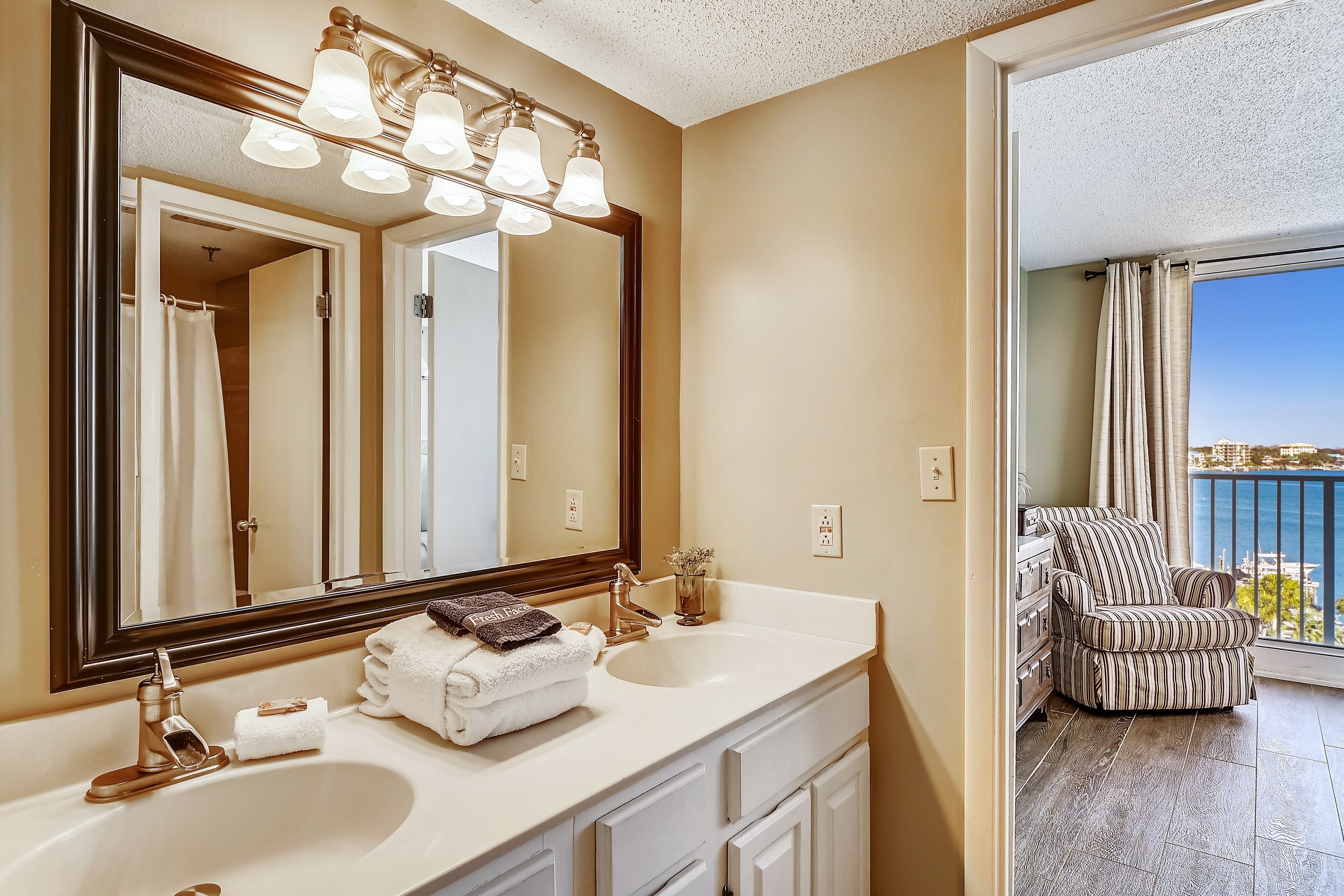 A bathroom with a large mirror, two sinks, and a chair by a balcony with a view.