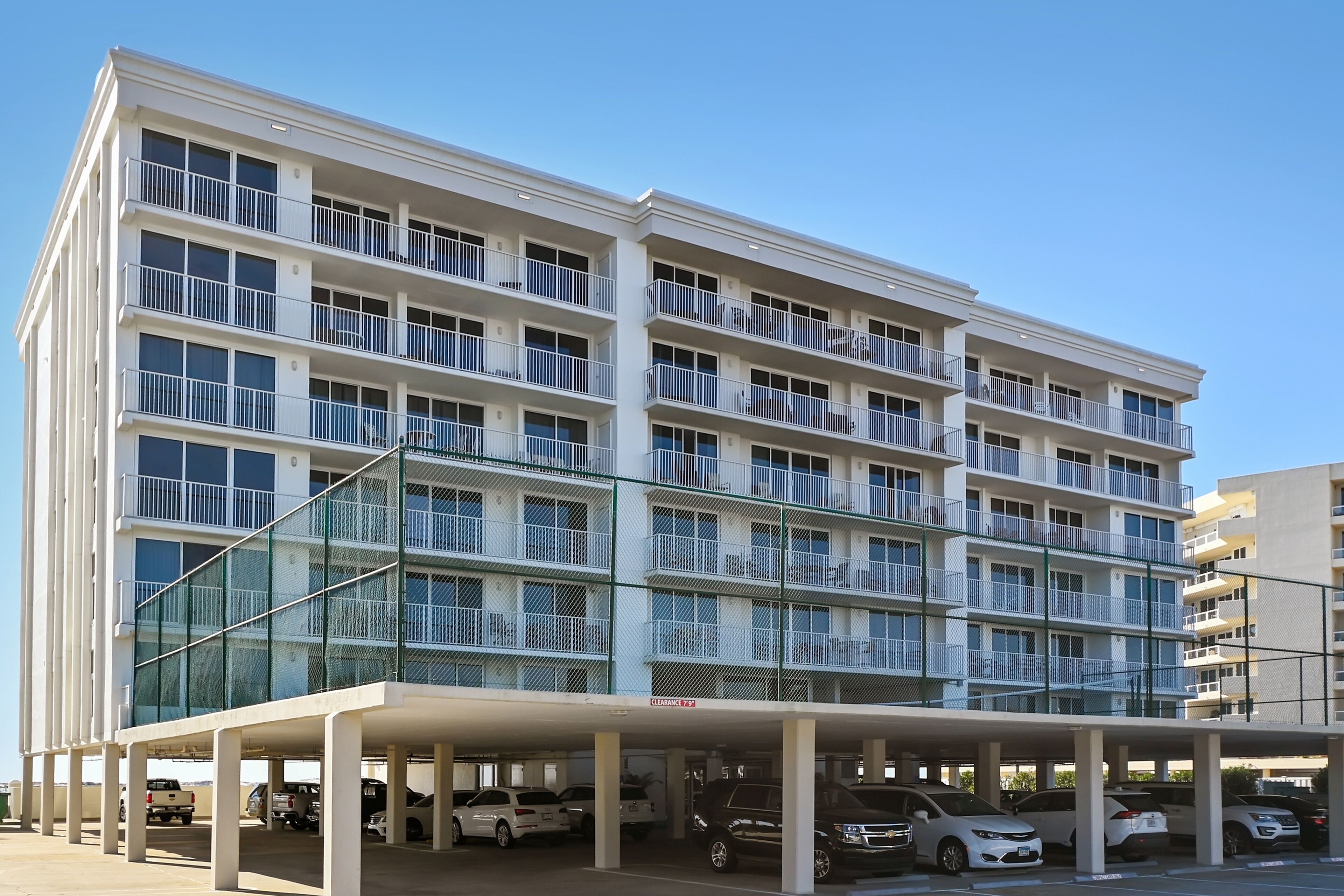 A multi-story hotel with balconies, a covered parking area, and several cars parked.
