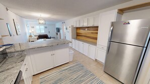 A modern kitchen with white cabinets, a stainless steel refrigerator, granite countertops, and a wooden backsplash. - Steps to the Pool 1 Bedroom Sleeps 4 by RedAwning (Fort Walton Beach)