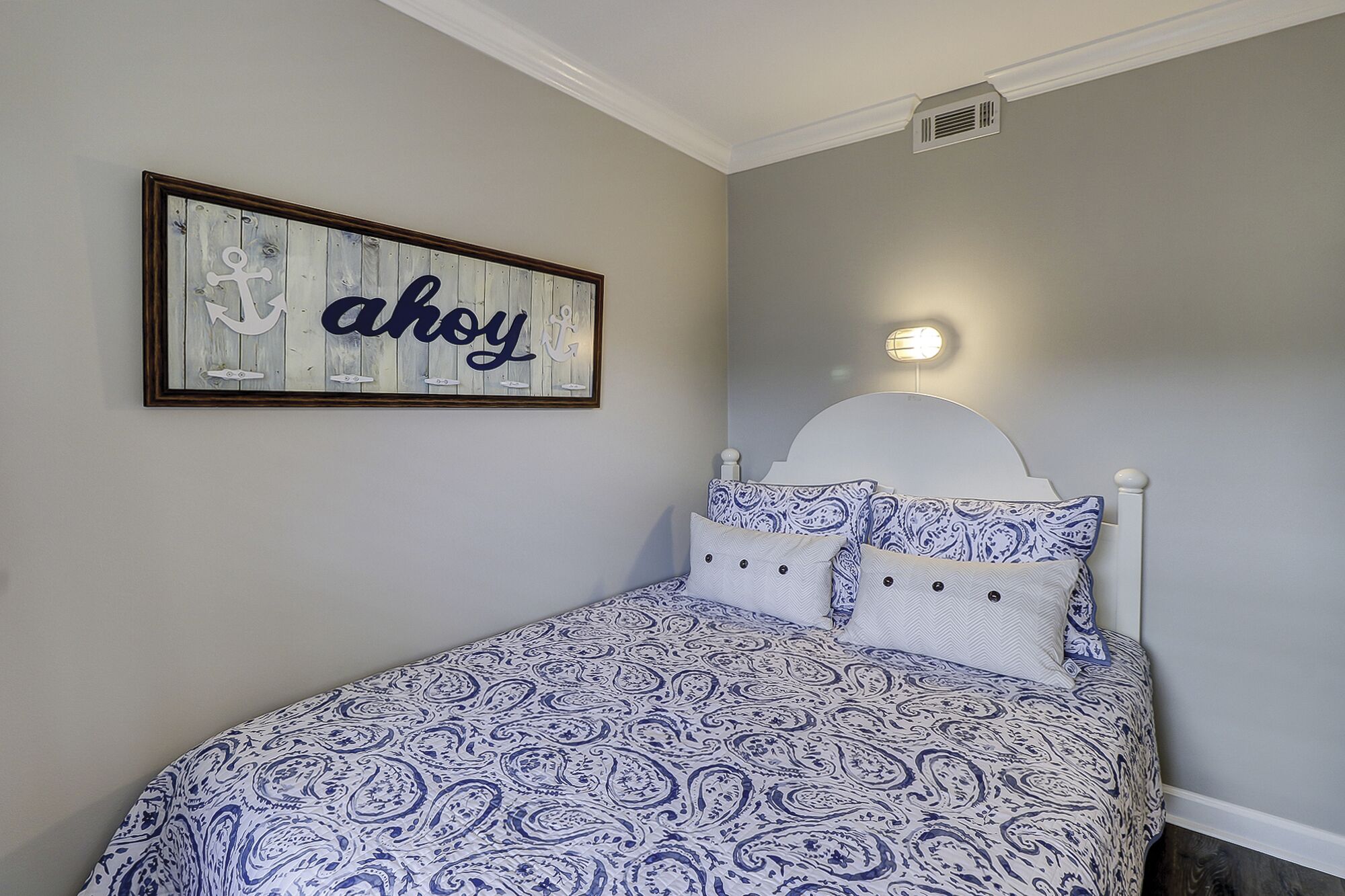 Une chambre à coucher avec un lit, une lampe fixée au mur et un panneau encadré portant le mot « ahoy ».
