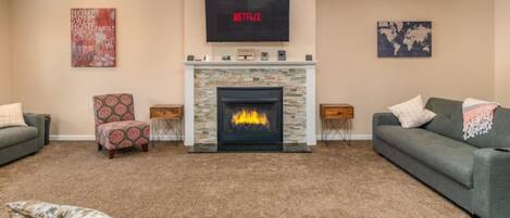 Una sala de estar con chimenea, televisor montado encima y dos sofás.
