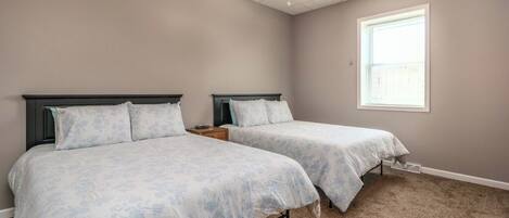 Une chambre avec deux lits, un ventilateur de plafond, une fenêtre et un revêtement de sol en moquette.