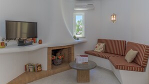 Un salon avec un téléviseur, des livres, une cheminée, un canapé et une petite table.