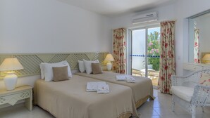 Une chambre d’hôtel avec deux lits, un balcon, une chaise et un appareil de climatisation.