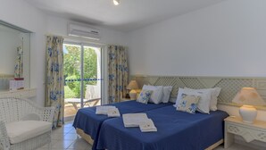 Ein Hotelzimmer mit zwei Betten, einer Sitzecke mit einem Sessel, einem Fenster mit Vorhängen und einem Nachttisch mit Lampe.